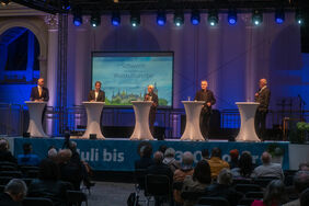 Dr. Badrow, Dr. Badenschier, Birgit Hesse, Joachim Brenncke und Jürgen Hingst stehen jeweils hinter einem Podium gemeinsam auf einer Bühne vor Publikum. Frau Hesse spricht in ihr Mikrophon. 