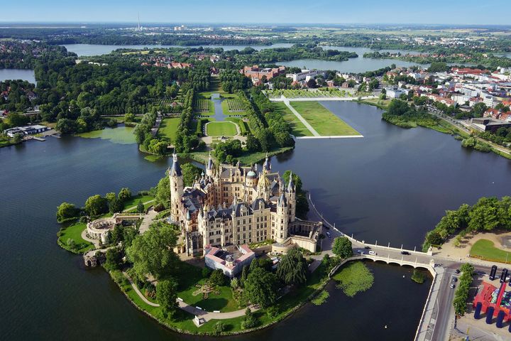 Das Schweriner Schloss und der Schlossgarten aus der Vogelperspektive an einem sonnigen Tag.