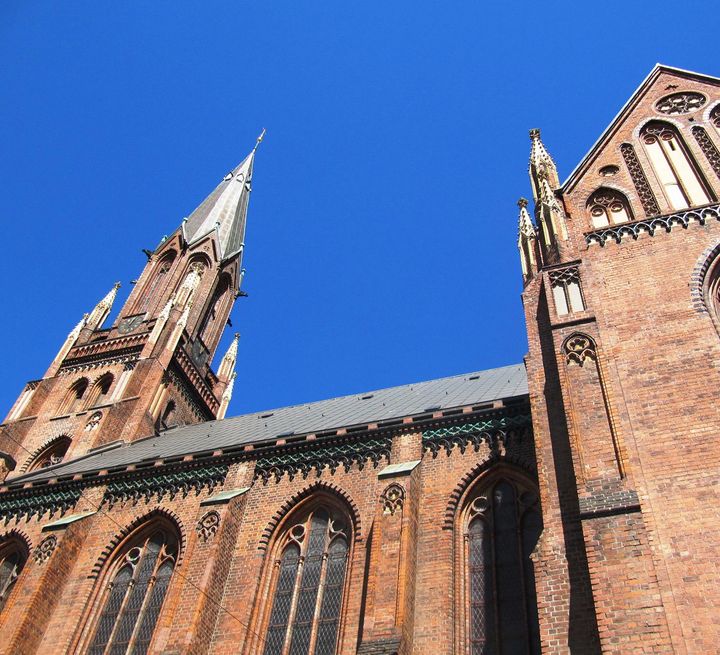 In einer Nahaufnahme der neugotische Paulskirche im schrägen Winkel aus Fußgängerperspektive zeigt sich ein starker Farbkontrast zwischen den braunen Backsteinen und dem blauen wolkenfreien Himmel.