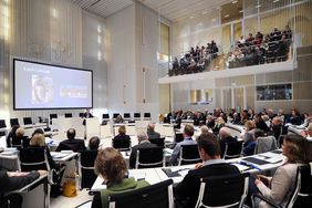 Im Plenarsaal des Schweriner Landtagsgebäudes spricht ein Herr vor einem Publikum an im Halbkreis ausgerichteten Tischreihen und auf der Publikumstribühne.
