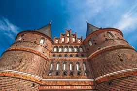 Das Lübecker Holstentor aus roten Backsteinen im spätgotischen Stil vor einem blauen Himmel. Es trägt die lateinische Inschrift concordia domi foris pax.