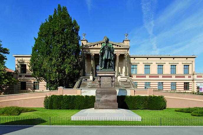  Die Frontansicht des Museums zeigt das Eingangsportal mit ionischen Säulen und einer großen Treppe. Im Vordergrund steht das Paul-Friedrich-Denkmal, eine Kupferstatue des Großherzogs auf einem Steinsockel. 